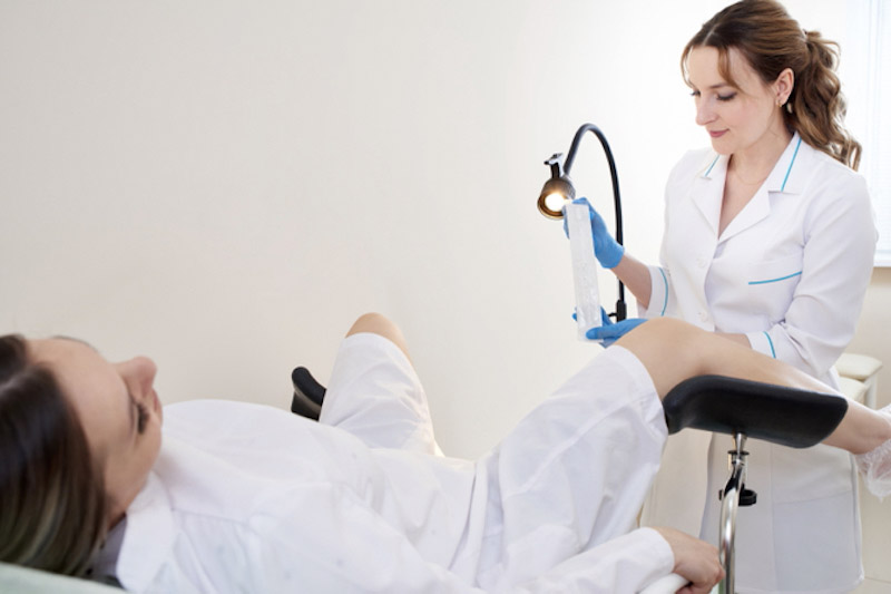 Paziente donna sdraiata su una poltrona di una clinica con gambe divaricate mentre la ginecologa si prepara ad effettuare il tampone vaginale